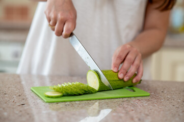 Close-up of hands slicing zucchini with a knife on a green board, concept: fresh meal preparation...