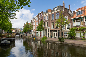A serene canal in Leiden the Netherlands, framed by historic brick houses and green trees, with a distant bridge under a partly cloudy sky.