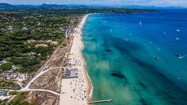 aerial view along Pampelonne Beach landscape to Saint-Tropez - located at coastline of Ramatuelle, C&ocirc;te d&rsquo;Azur, France - with people on the beach in water, green wooded hilly landscape in background