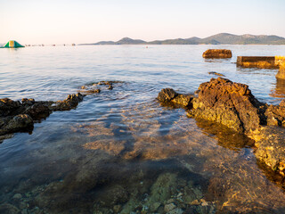 Volcanic coastal rocks in Biograd na Moru, Croatia, glowing in warm sunrise light with calm Adriatic Sea and distant mountains in the background.