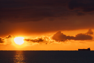 Ocean sunset with commercial shipping vessel silhouetted against golden sky. Stunning seascape showing the sun's reflection creating a light path on the water.