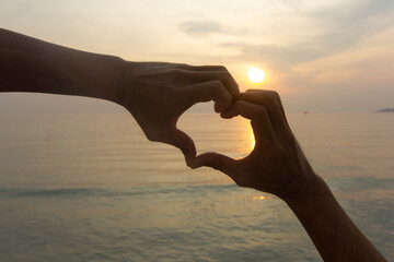 silhouette man hands making heart shape  at sunset on the sea , love concept	