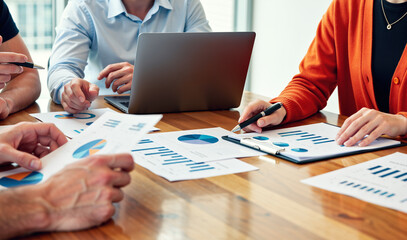Team Reviewing Printed Reports and Laptop Screen Together at Collaborative Meeting Table. Collaborative Data Review.