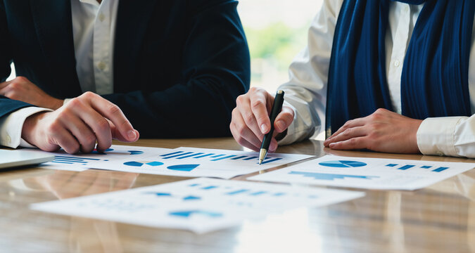 Two Colleagues Pointing at Printed Charts and Discussing Figures at Conference Table