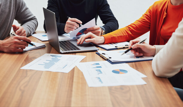 Team Reviewing Printed Reports and Laptop Screen Together at Collaborative Meeting Table. Collaborative Data Review.