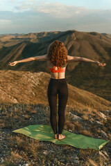 A woman practices yoga on a mat atop a mountain