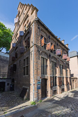 Historic brick Besiendershuis building in Nijmegen with brown shutters on a sunlit cobblestone street, showcasing classic Dutch architecture and a serene urban scene.