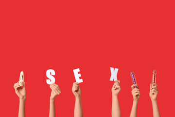 Female hands with word SEX and vibrators on red background