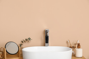 Modern sink with bath supplies and mirror on countertop near brown wall in bathroom