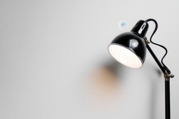 A sleek black desk lamp illuminating a minimalist workspace with a soft shadow on the wall
