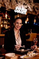 Smiling Woman Enjoying Sushi in Elegant Restaurant with Wine and Cozy Atmosphere