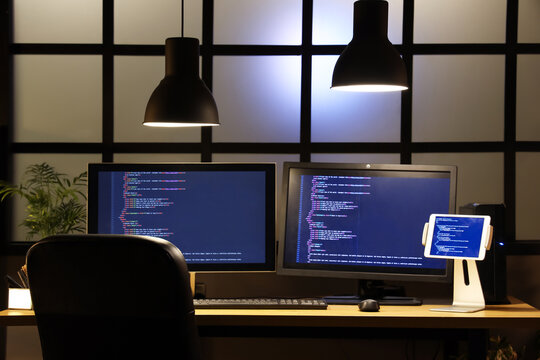 programmer's desk with computer monitors and tablet in dark office at night