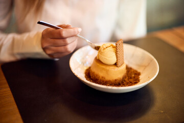 Person Enjoying Caramel Dessert with Ice Cream and Biscuit Topping in a Bowl