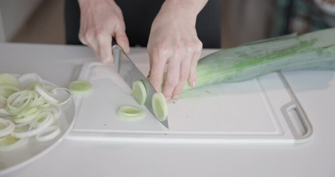 Home cooking - woman in small apartment cutting fresh organic leek with santoku knife on vegetable cutting board
