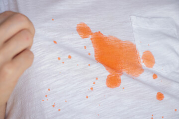 White T-shirt with orange stain and girl showing stain, pulling fabric with hand on washing, dirt...