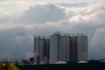 Large industrial facility with tall storage silos and smoky urban backdrop