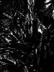 Transparent cellophane bag against a sleek black background, showcasing its glossy, delicate texture. The wrinkled and tattered plastic surface creates an intriguing abstract pattern, highlighting.