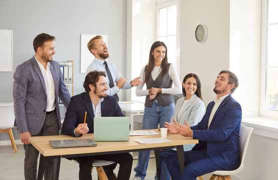 Cheerful business team gathered around office table laughing and enjoying friendly conversation. Happy colleagues sharing ideas, discussing projects and building positive work relationships in office.