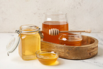 Wooden tray with jars, bowl and glass of sweet honey on white grunge table