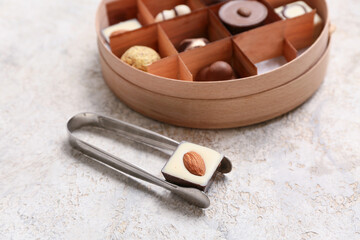 Kitchen tongs with delicious chocolate candy on light background