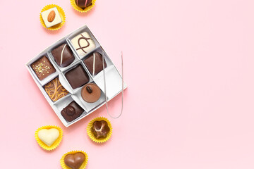 Box with candies and kitchen tongs on pink background