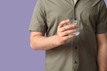 Fototapeta premium Young man with glass of clean water on lilac background