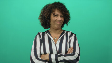 Hispanic woman crossing arms and scrunching face while wearing striped shirt in green studio;...