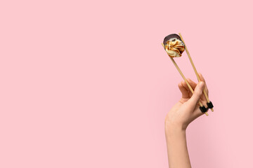 Hand with tasty sushi roll and chopsticks on pink background