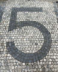 The number five written out of cobblestones on a cobblestone street.