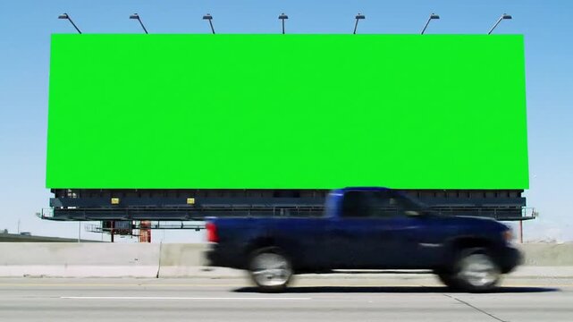Highway advertising concept featuring a large blank green screen billboard with a speeding pickup truck passing on the freeway.
