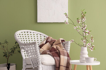 White armchair and vase with blooming branches on coffee table near green wall