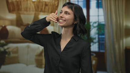 Obraz premium Woman holds hand in call gesture inside a modern living room building while smiling broadly; playful joy.