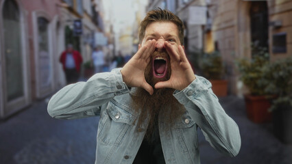 Man with long beard shouting loudly and cupping hand to mouth on a busy city street under daylight;...