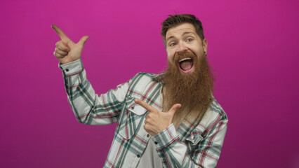Man pointing finger in studio with expressive smile and plaid shirt against pink wall; excitement fun energy.
