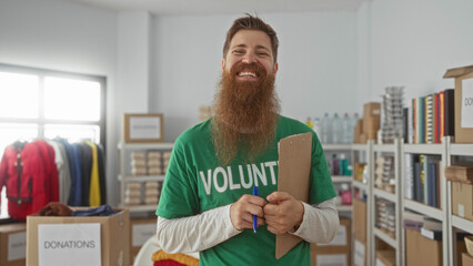 Man smiling while writing on clipboard in building surrounded by donation boxes and shelves; charity spirit.