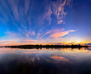 Sunset reflected in the river. Orange and pink fan clouds scatter. Calm evening river reflects the...