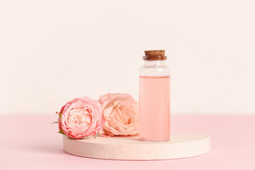 Bottle of cosmetic oil, roses and plaster stand on pink background