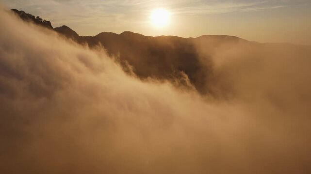 Drone video of mountain peaks surrounded by golden clouds at sunset, with warm light illuminating the misty slopes in Spain.