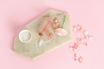 Composition with bottles of cosmetic oil, sea salt, petals and rose on pink background