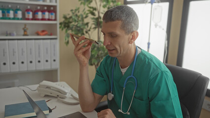 Doctor in clinic uniform using smartphone for voice message in hospital office with stethoscope...
