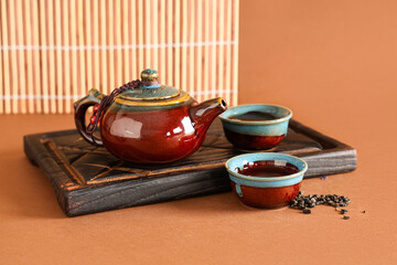 Wooden tray with teapot, cups and dry tea on brown background