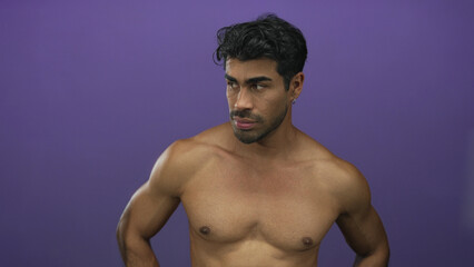 Fototapeta premium Man bare muscular chest looking down with hands on hips in a studio against a purple wall; contemplation.