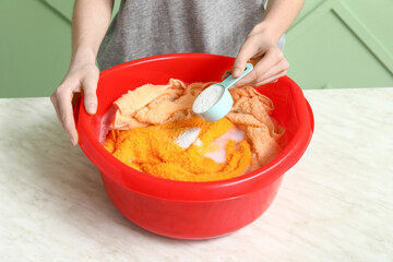 Woman adding detergent to clothes in plastic basin on table against green background