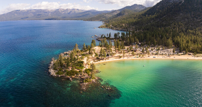 Aerial view of crystal-clear turquoise waters meet the sandy shores beneath the towering pines, a vibrant contrast against the backdrop of distant mountains, Sand Harbour Beach, Nevada, United States. - Powered by Adobe