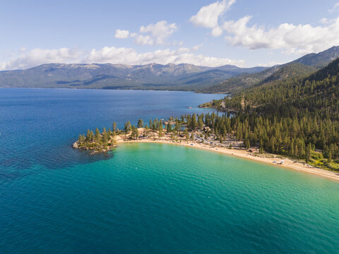 Aerial view of the turquoise waters meeting the sandy shores of Incline Village, with a backdrop of lush green forests and distant mountains, Incline Village, Nevada, United States.