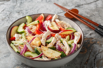 Diet salad with shredded chicken, cucumber, apple, red onion, bell pepper and sesame seeds in Asian style close-up in a bowl on the table. Horizontal