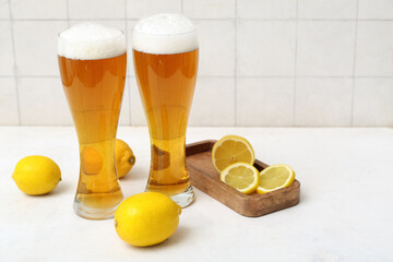 Glasses of fresh beer and wooden board with lemons on white table