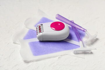 Modern epilator with razors and wax strips on white grunge background