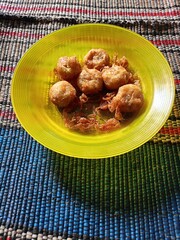 Close-up view from above of a transparent yellow plastic plate with cooked dumplings served on a mat.