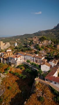 Drone video of the historic hilltop village of Guadalest in Spain, showcasing its ancient castle, charming houses, and surrounding mountains under clear blue skies.